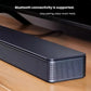 A close-up angle of the Bose TV Speaker on a wooden surface, highlighting its premium grille and build quality, with text emphasizing its easy Bluetooth pairing for wireless music.