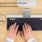 Hands typing on the Logitech K780 while a smartphone rests in the keyboard’s rubber cradle, emphasizing large low-profile keys and ergonomic layout for everyday productivity.